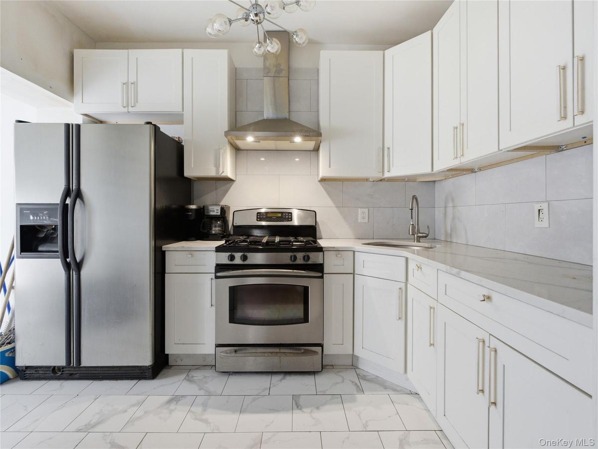 Kitchen with appliances with stainless steel finishes, light marble finish floors, wall chimney exhaust hood, and white cabinetry
