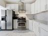 Kitchen with appliances with stainless steel finishes, light marble finish floors, wall chimney exhaust hood, and white cabinetry