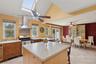 Kitchen with light tile patterned floors, wall chimney exhaust hood, a kitchen island, stainless steel range with gas cooktop, and a skylight