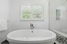 Spa-inspired primary bath featuring a freestanding oval soaking tub, marble-look wall tile surround, polished stone-look flooring with geometric mosai