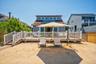 Expansive sandy backyard featuring a wooden deck with white railing, direct access to the interior, and a wooden walkway