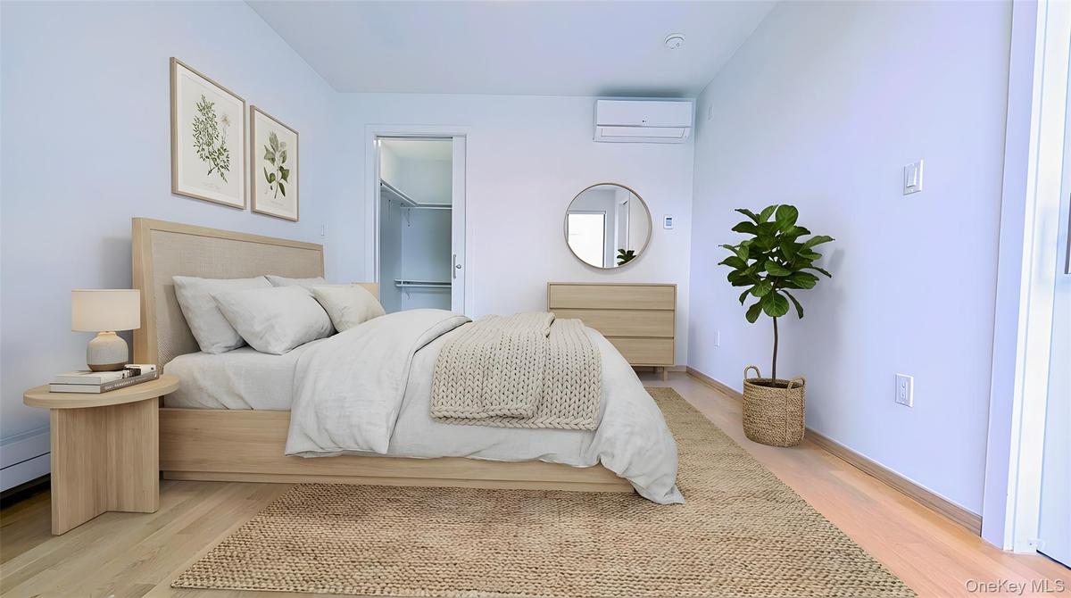 Bedroom featuring a walk in closet, a wall mounted air conditioner, and light wood-style flooring