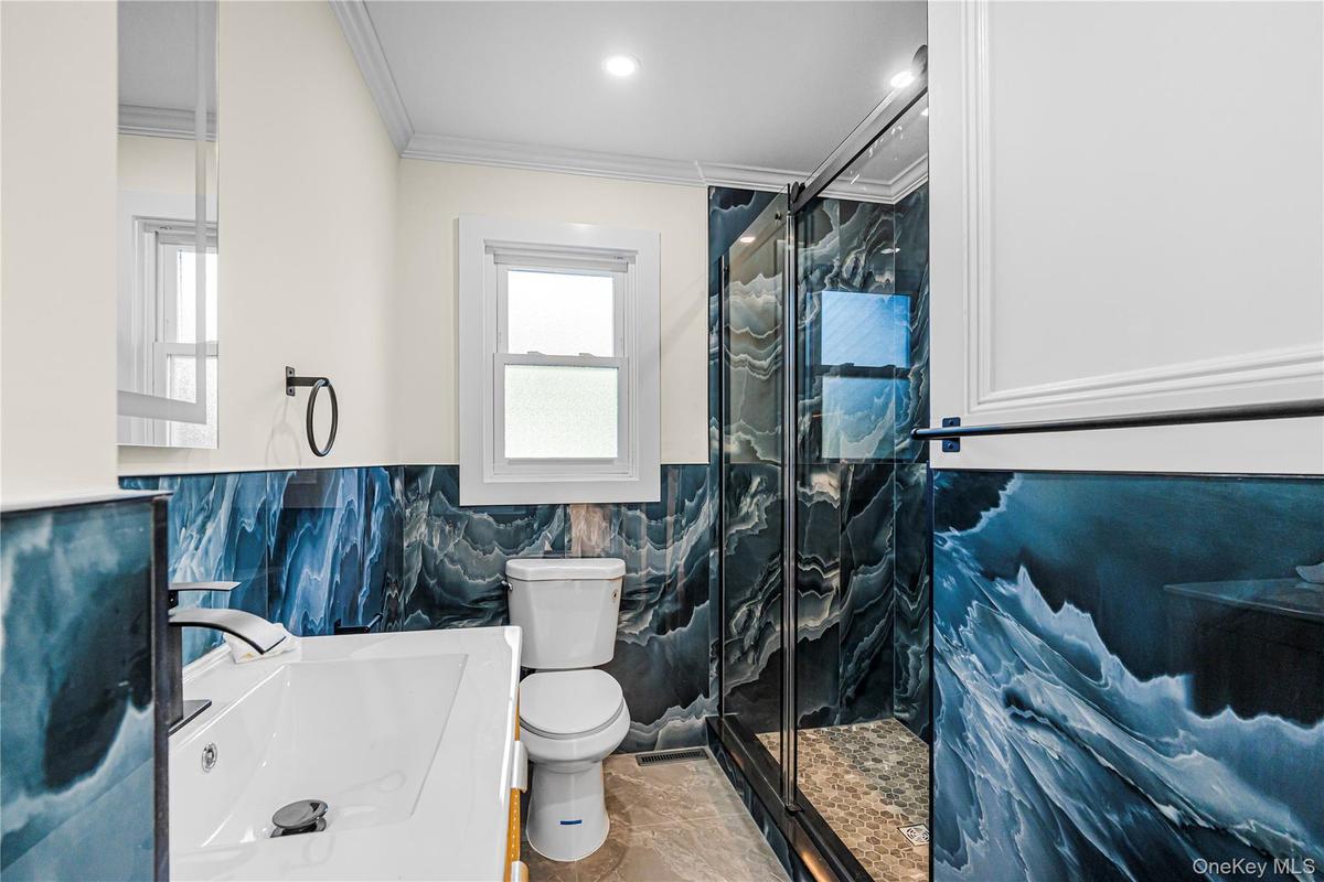 Bathroom featuring blue wave-patterned wall tiling, a glass-enclosed shower with a pebble-tiled floor, and a white vanity with a single basin and a ma