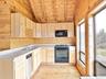 Kitchen featuring light brown cabinetry, black appliances, lofted ceiling, wooden ceiling, and wooden walls