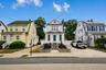 White clapboard exterior with an arched dormer, raised stone planter beds, and a concrete driveway