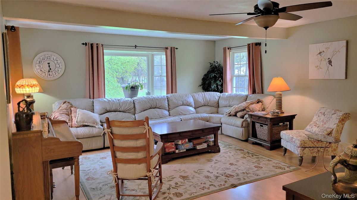 Spacious living area featuring light-toned walls, wood-finish flooring, and a ceiling fan with integrated lighting