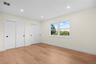 Spacious room featuring wood-finish flooring, two sets of bi-fold closet doors with black hardware, a large window, recessed lighting, and white baseb