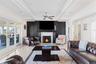 Living room featuring inlaid floor details, a warm lit fireplace, ceiling fan, crown molding, and beamed ceiling