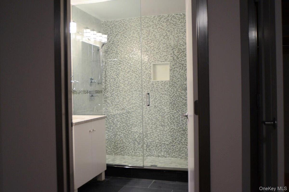 Bathroom with a shower stall, vanity, and dark tile patterned flooring