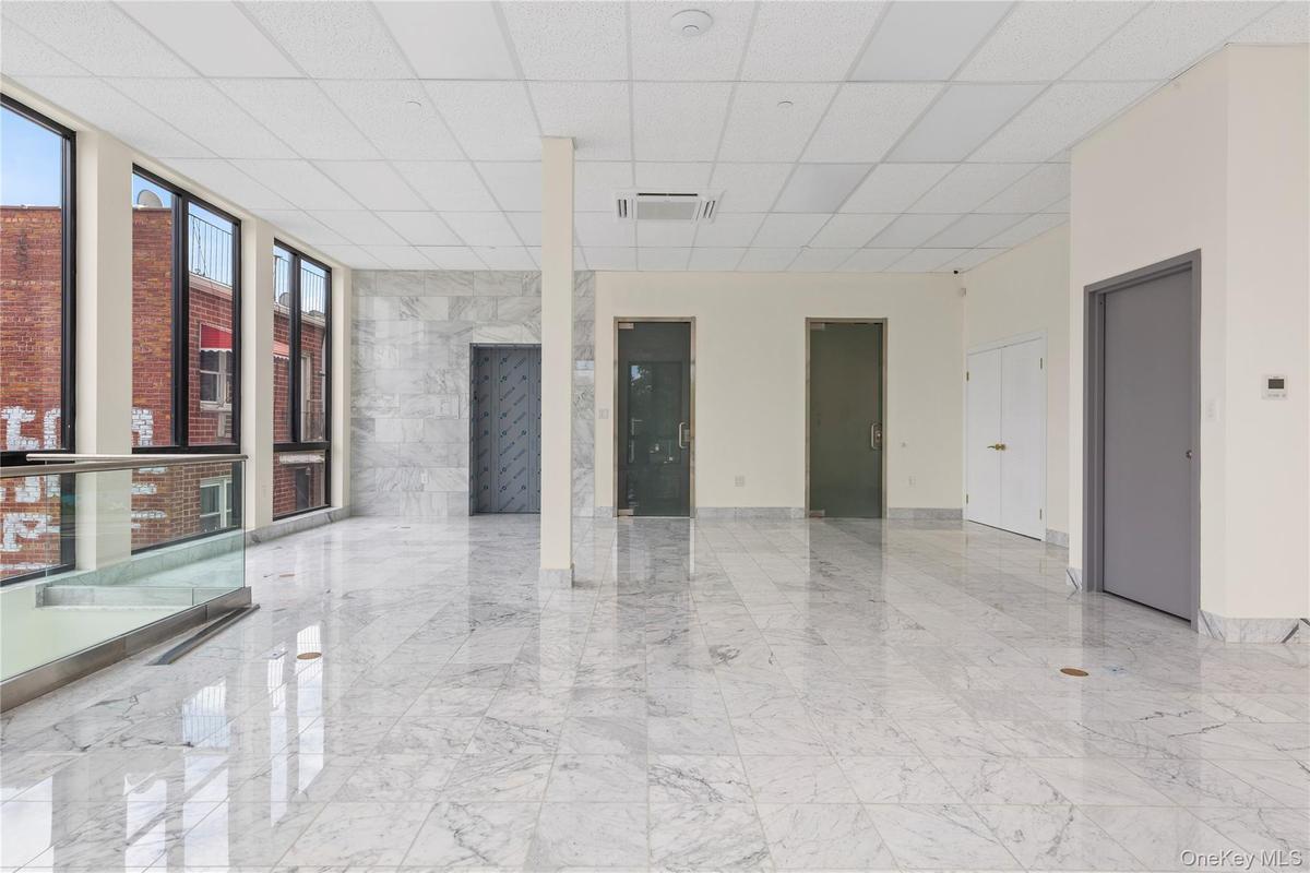 Empty room featuring marble tiled flooring, a drop ceiling, and expansive windows
