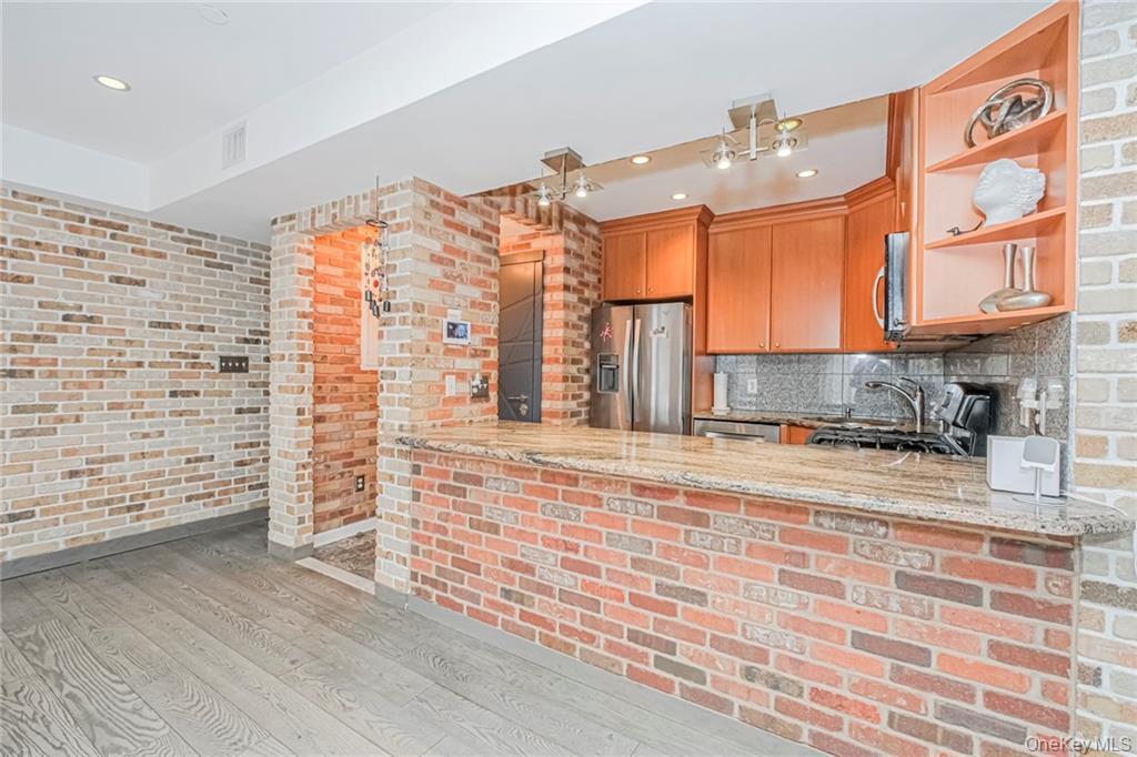 Kitchen with brick wall, light stone counters, light wood-style floors, stainless steel appliances, and a peninsula