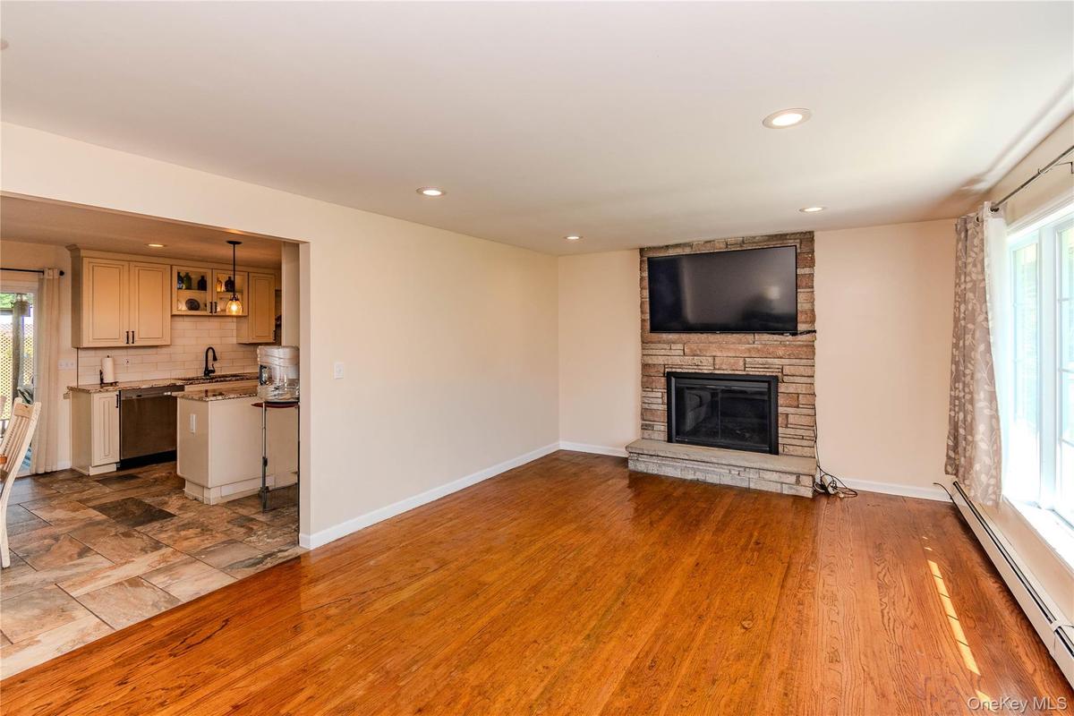 Hardwood flooring, recessed lighting, stone-clad fireplace, large window, and an open pass-through to the kitchen