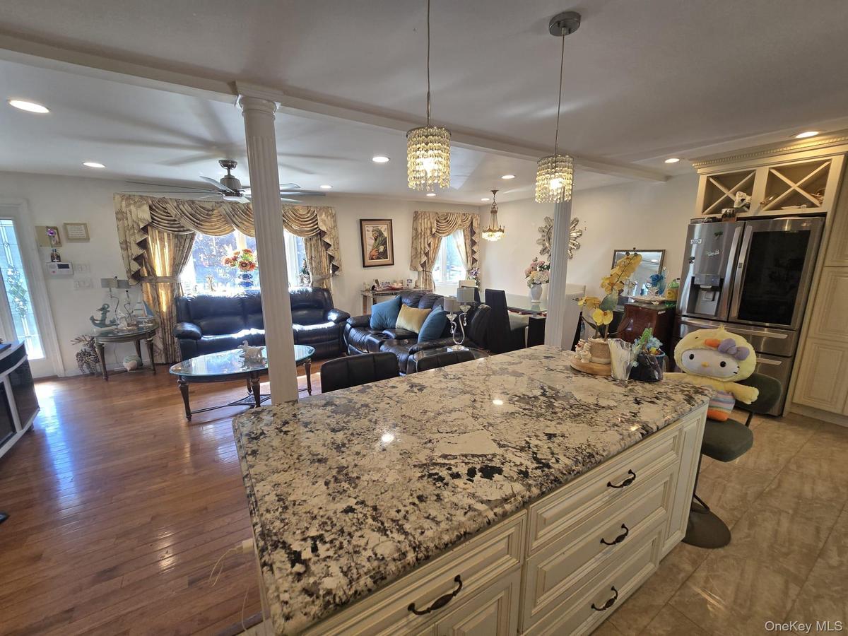 Spacious open-concept interior featuring a large kitchen island with a speckled countertop and cream-colored cabinetry, two crystal pendant lights, re