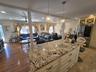 Spacious open-concept interior featuring a large kitchen island with a speckled countertop and cream-colored cabinetry, two crystal pendant lights, re