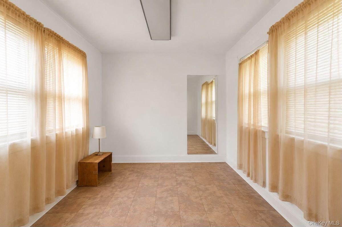 Room featuring light-toned flooring, white walls, and two large windows with blinds and sheer curtains