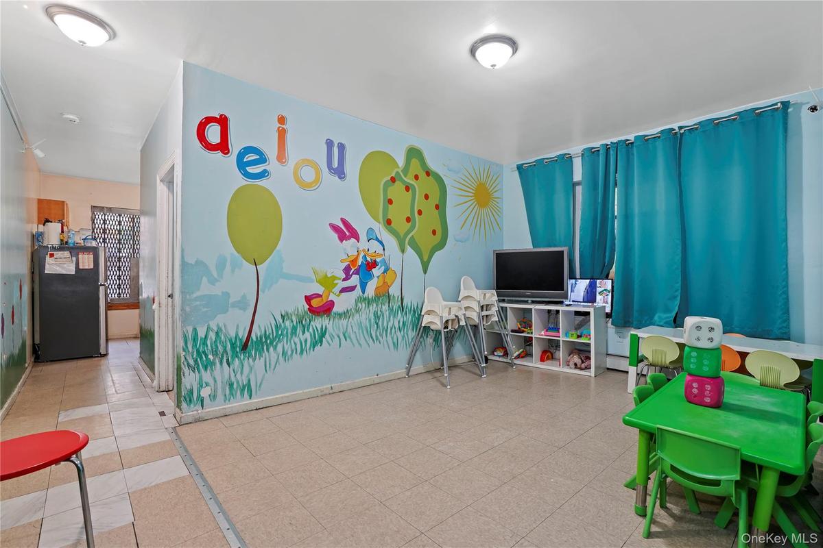 Spacious room featuring light-colored square floor tiles, a built-in wall mural, and multiple windows with teal curtains