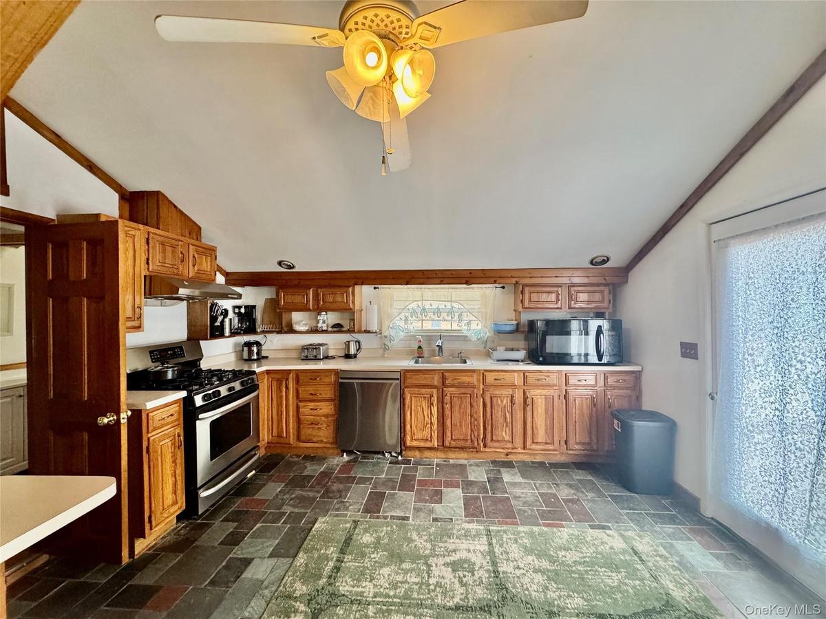 0 - Kitchen featuring light countertops, stainless steel appliances, a sink, a ceiling fan, and stone finish flooring