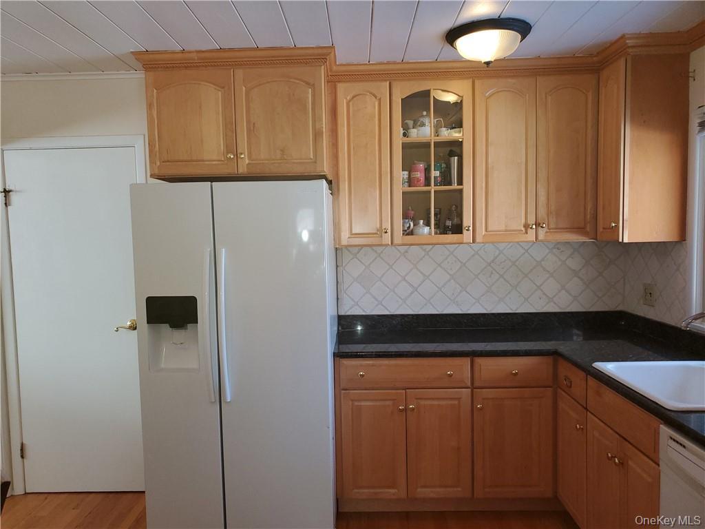 Kitchen featuring dark countertops, white appliances, glass insert cabinets, a sink, and backsplash