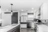 Modern kitchen featuring white cabinetry, a large center island with a white and black veined countertop, stainless steel appliances, wood-finish floo