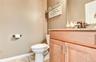 Bathroom featuring a light wood-finish vanity with paneling and brushed nickel hardware, a granite countertop, and a built-in sink with a dark-toned f