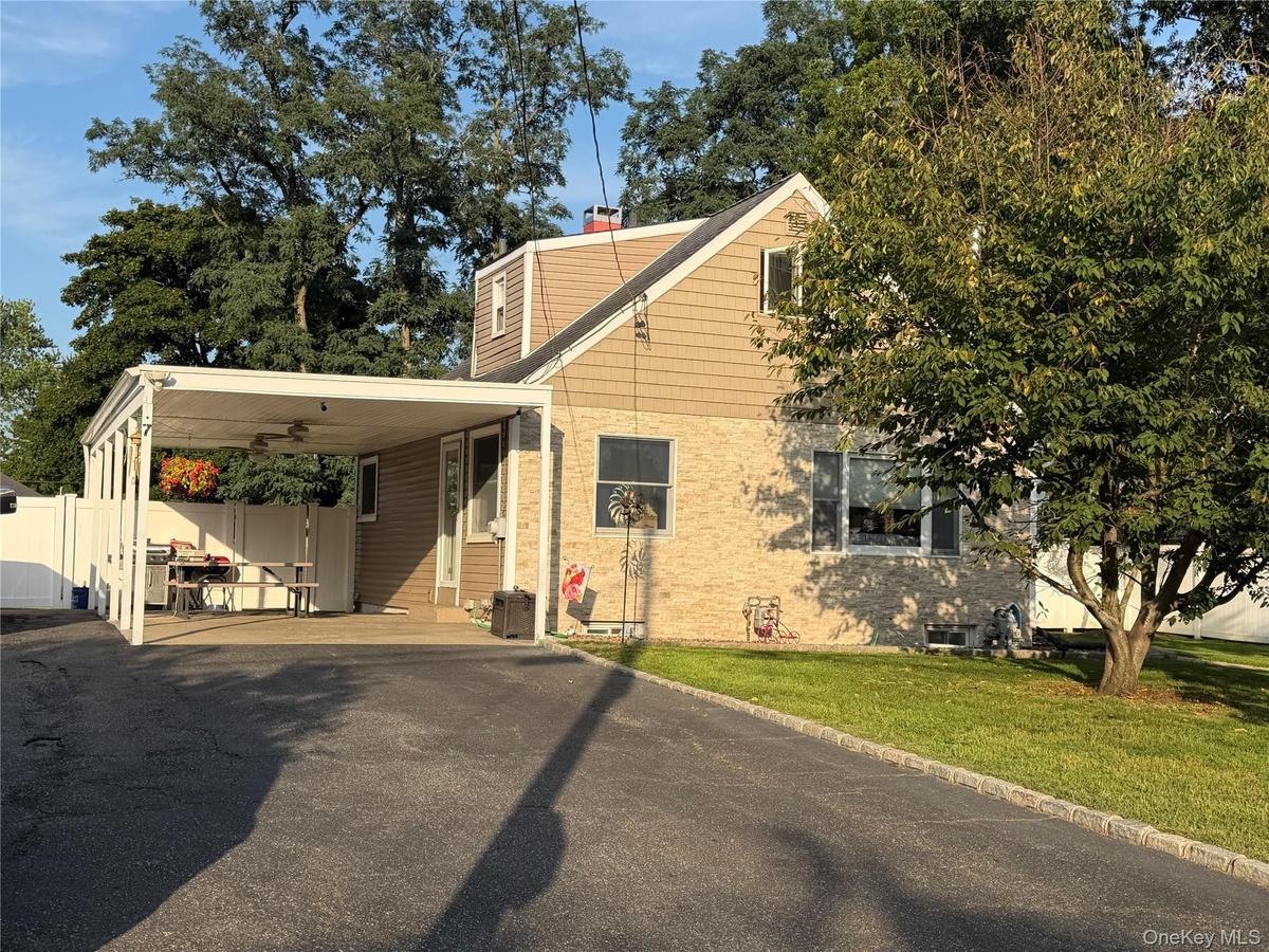 Two-story residence featuring brick and siding exterior, an attached carport with ceiling fans, a paved driveway, and a white privacy fence