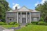 Greek revival inspired property featuring a standing seam roof, brick siding, a metal roof, a chimney, and a front yard