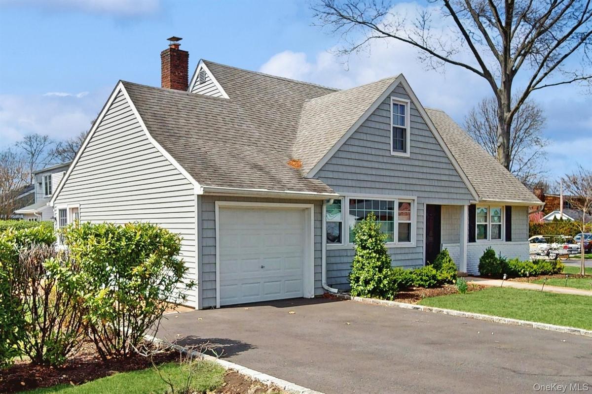 New england style home with a garage, driveway, a chimney, and a shingled roof