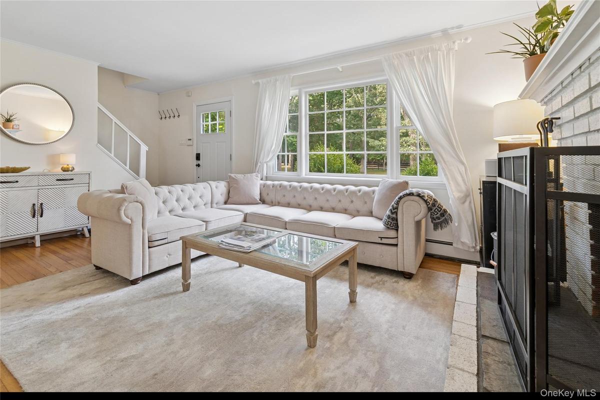 Living area featuring a brick fireplace, stairs, a baseboard radiator, light wood-type flooring, and crown molding
