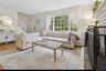 Living area featuring a brick fireplace, stairs, a baseboard radiator, light wood-type flooring, and crown molding