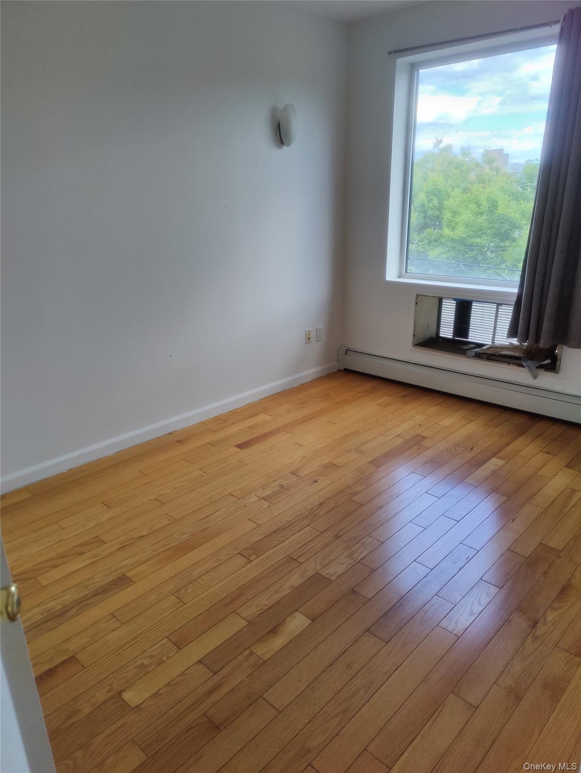 Empty room with baseboard heating and light wood-style floors
