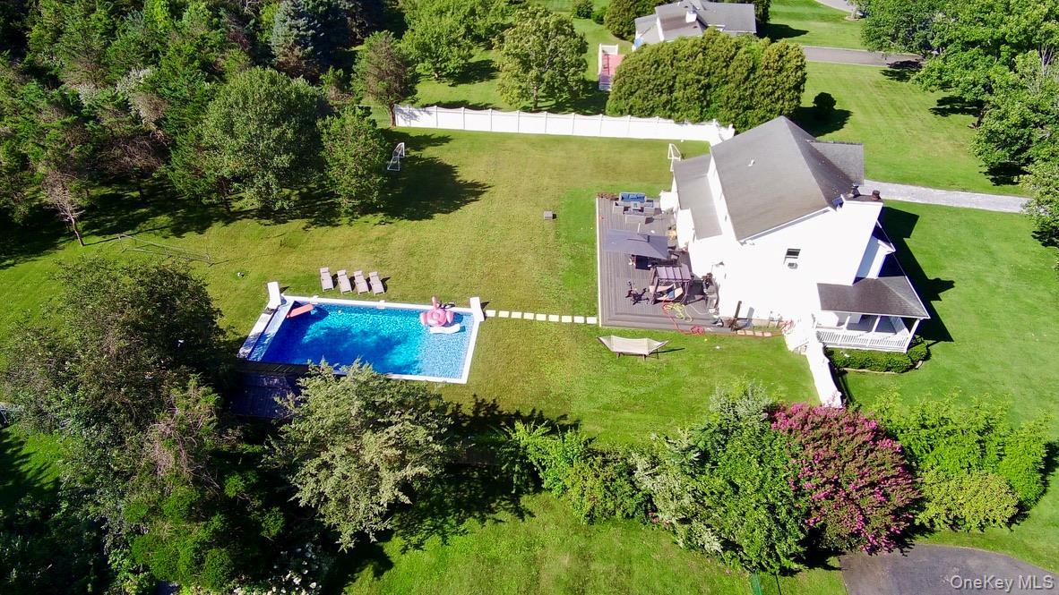 Expansive green lawn featuring an in-ground swimming pool, a large outdoor patio, mature trees, and a white picket fence.