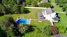Expansive green lawn featuring an in-ground swimming pool, a large outdoor patio, mature trees, and a white picket fence.