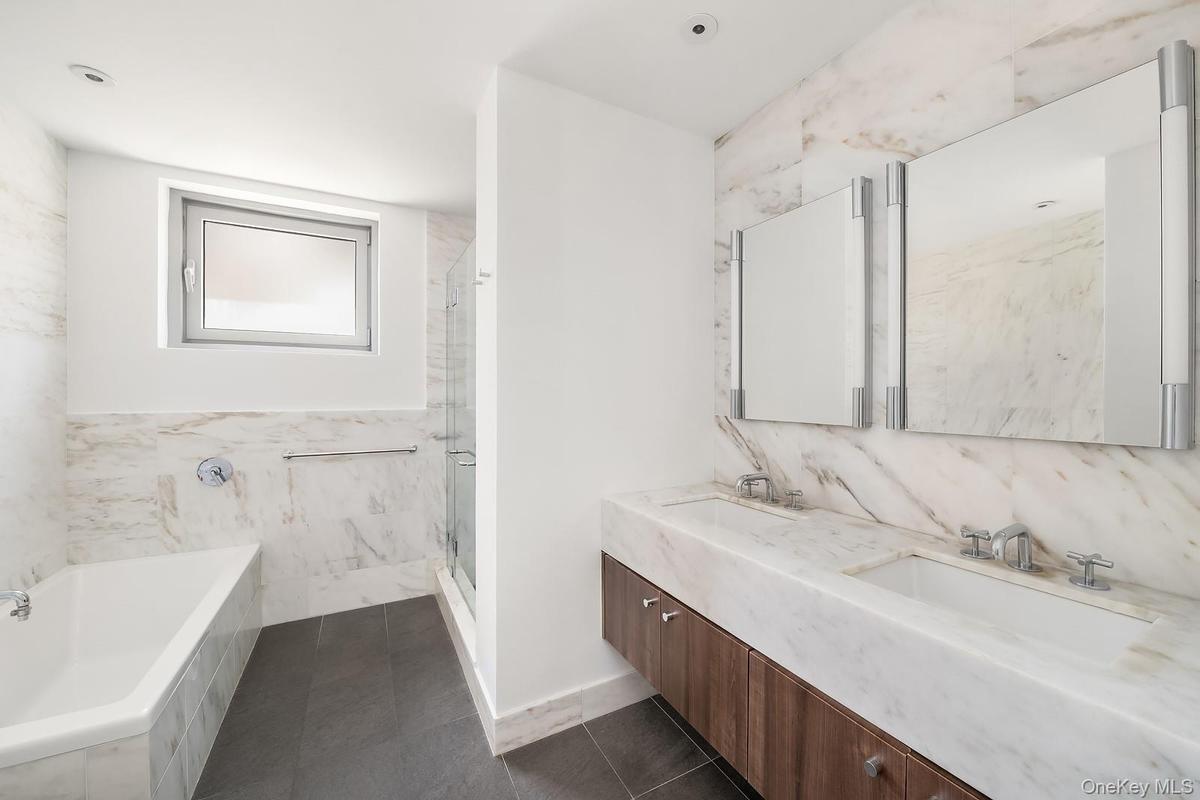 Bathroom featuring a floating double vanity with integrated sinks and a wood-finish base, dual wall-mounted illuminated mirrors, and a full-height til