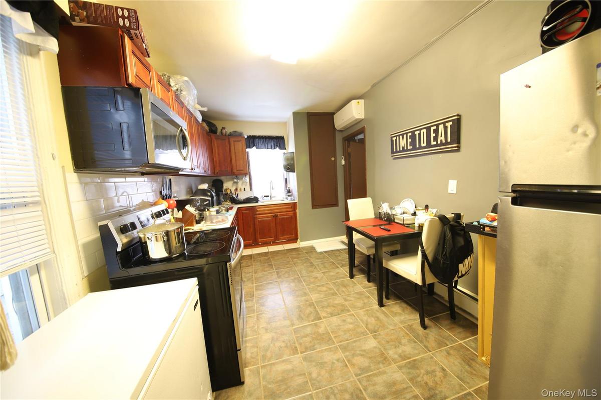 Kitchen featuring reddish brown cabinets, a wall mounted AC, tasteful backsplash, light tile patterned floors, and stainless steel appliances