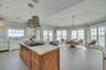 Kitchen with brown cabinetry, white cabinets, light stone counters, stainless steel gas stovetop, and a kitchen island