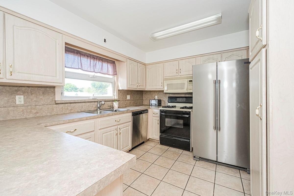 Kitchen featuring light-toned cabinetry with brass hardware, a stainless steel side-by-side refrigerator, a black electric range, and a stainless stee