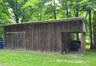 Wood-sided sheep barn featuring a sliding barn door and an attached open-sided storage area