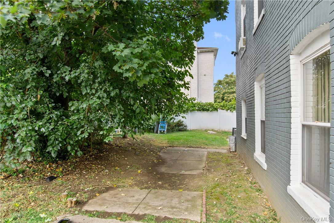 Side yard featuring a mature tree, concrete patio sections, and a privacy fence