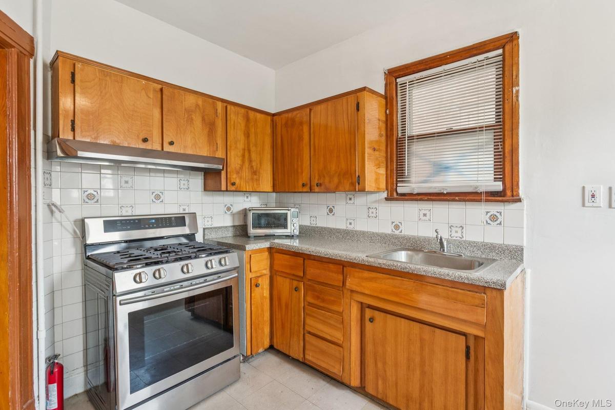 Kitchen featuring stainless steel range with gas cooktop, ventilation hood, tasteful backsplash, brown cabinets, and light tile patterned floors