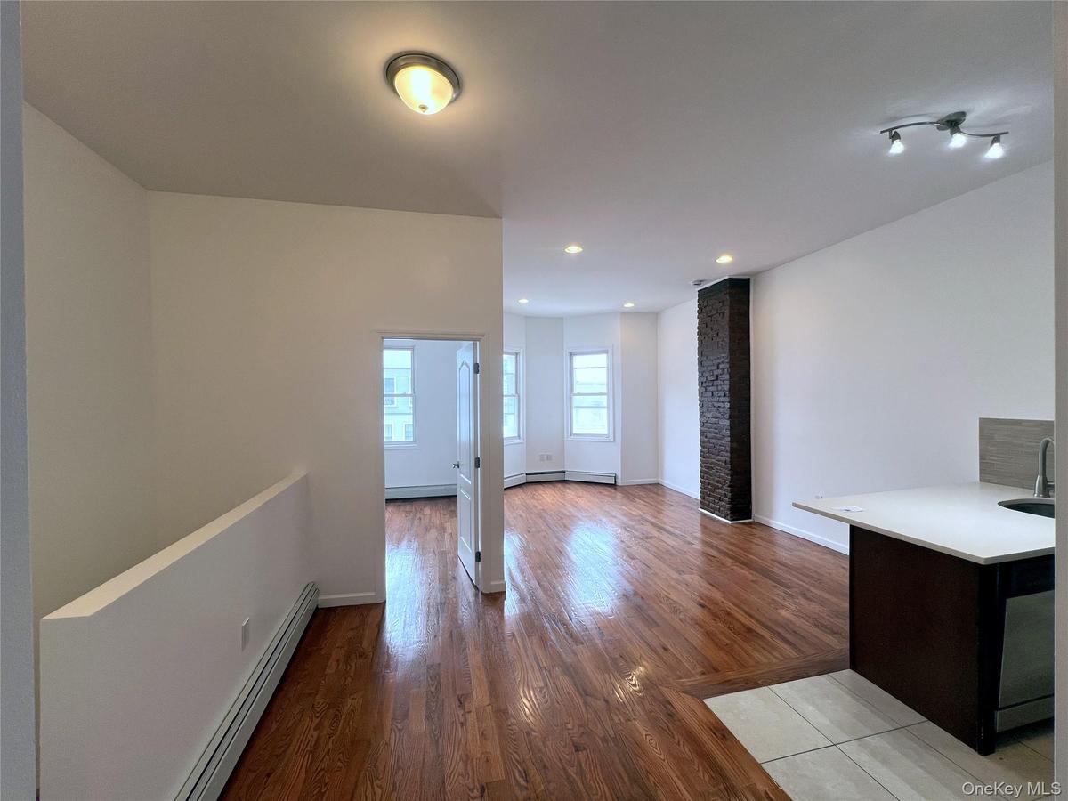 Unfurnished living room featuring a baseboard heating unit, light wood finished floors, and a stone fireplace