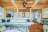 Open-concept living area featuring wood-finish flooring, exposed wooden beams, and a wood-slat ceiling with a ceiling fan