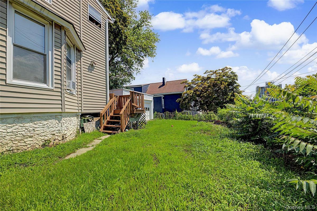 Vinyl siding exterior with a wood deck and staircase, featuring a concrete pathway and a grassy yard