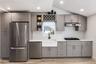 Stainless steel appliances, white subway tile backsplash, white farmhouse sink, grey shaker-style cabinetry, and wood-finish flooring
