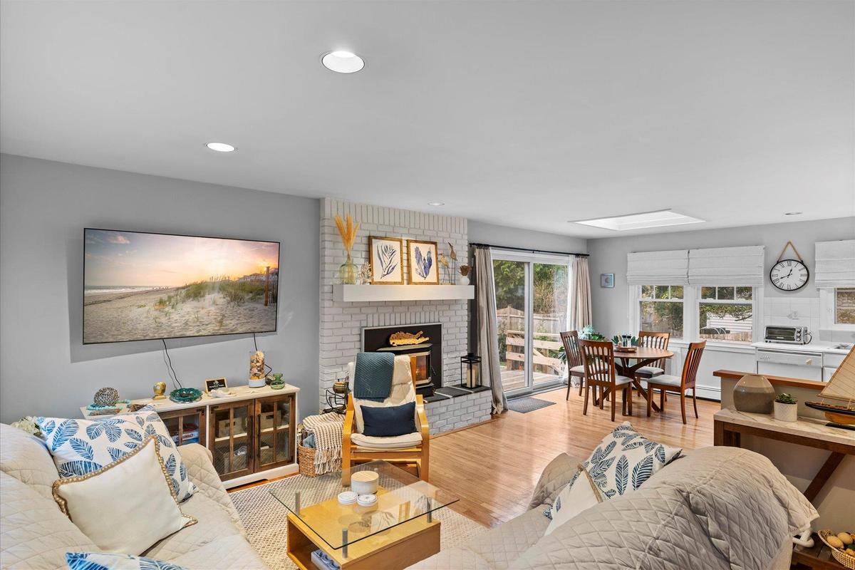 Living area with a skylight, a brick fireplace, wood finished floors, and recessed lighting