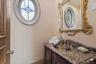Powder room featuring an oval window, ornate framed mirror, granite countertop, undermount sink, and decorative vanity cabinetry