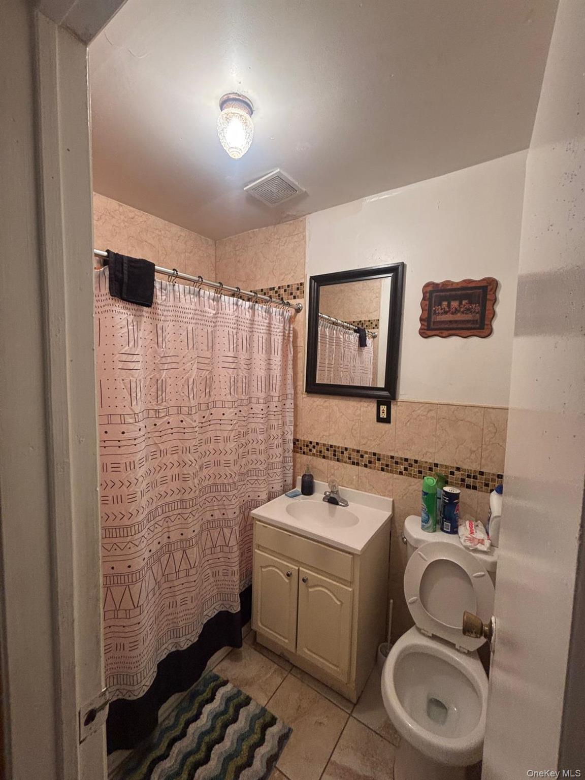 Bathroom with tile walls, vanity, a shower with curtain, light tile patterned floors, and wainscoting
