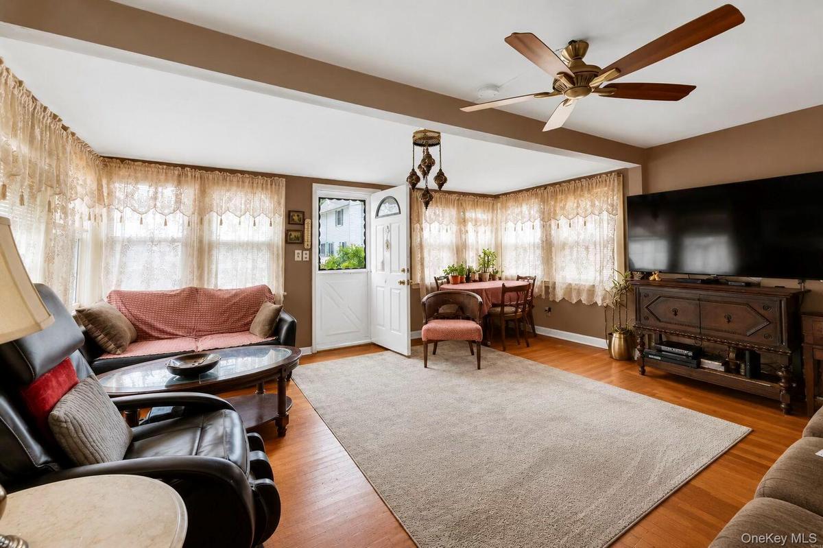 Spacious living area featuring wood-finish flooring, a ceiling fan with integrated lighting, and multiple windows