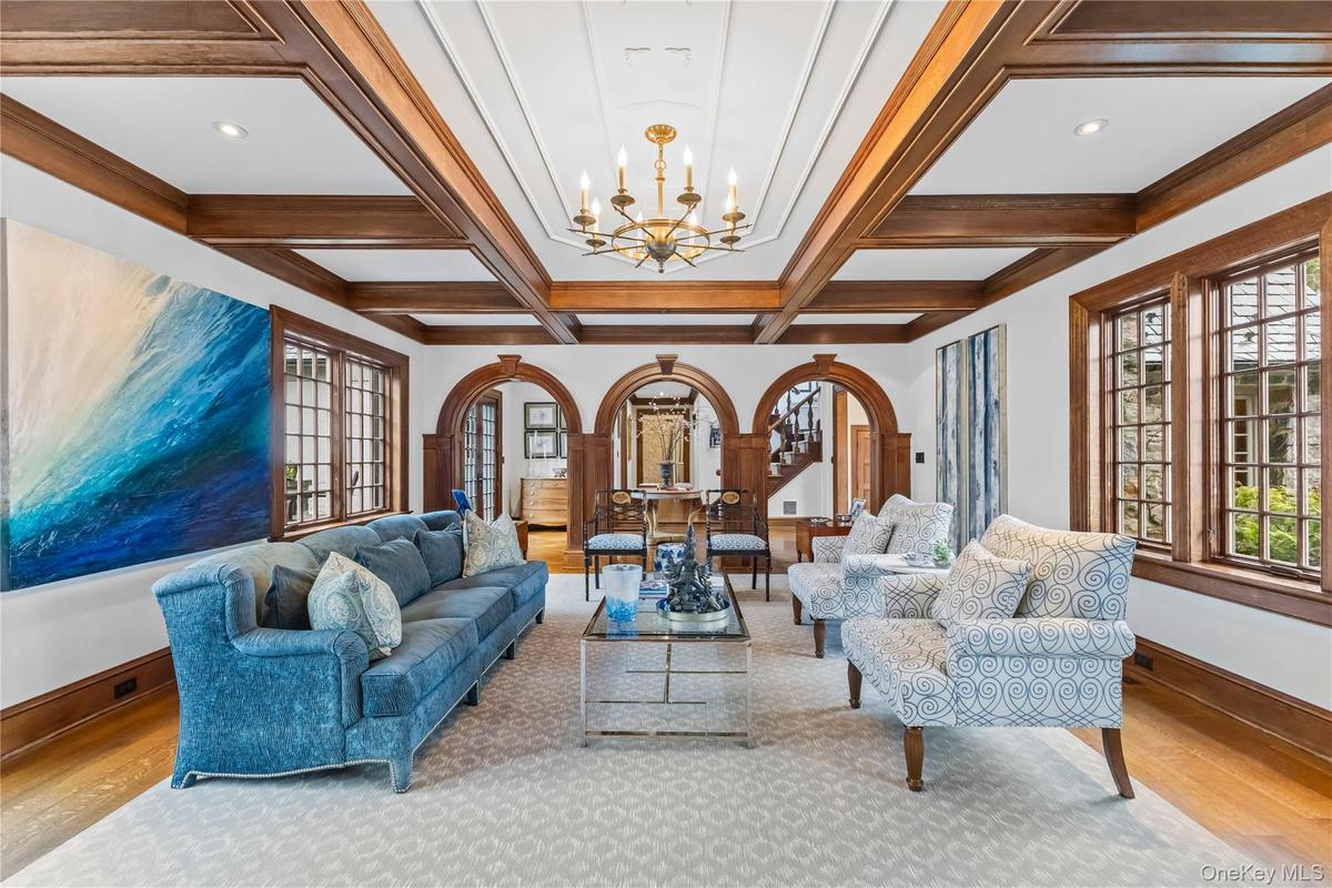 Stunning living room showcasing timeless architectural detail with a coffered ceiling, rich wood trim, elegant chandelier, and beautiful arched doorwa