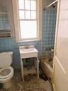Bathroom featuring a window, tile flooring, a toilet, a vanity with a sink, and a bathtub with tiled walls