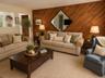 Living room diagonal wood accent wall with a diamond-shaped mirror, two sofas, an arm chair, coffee table, light color carpet and a view through into 